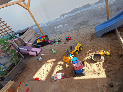 Großer, ebenerdiger Sandkasten mit kleiner Rutsche